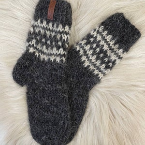 May include: A pair of gray and white knitted wool mittens with a brown leather tag. The mittens have a traditional Scandinavian pattern.