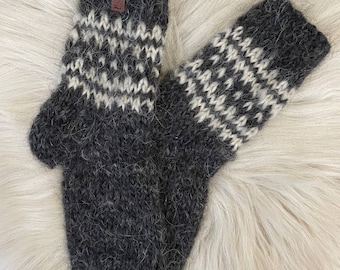 May include: A pair of grey and white knitted wool mittens with a brown leather tag. The mittens have a traditional Scandinavian pattern.
