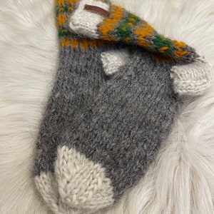 May include: A pair of grey, white and yellow knitted socks with a brown leather tag. The socks are made from a soft, fuzzy yarn.