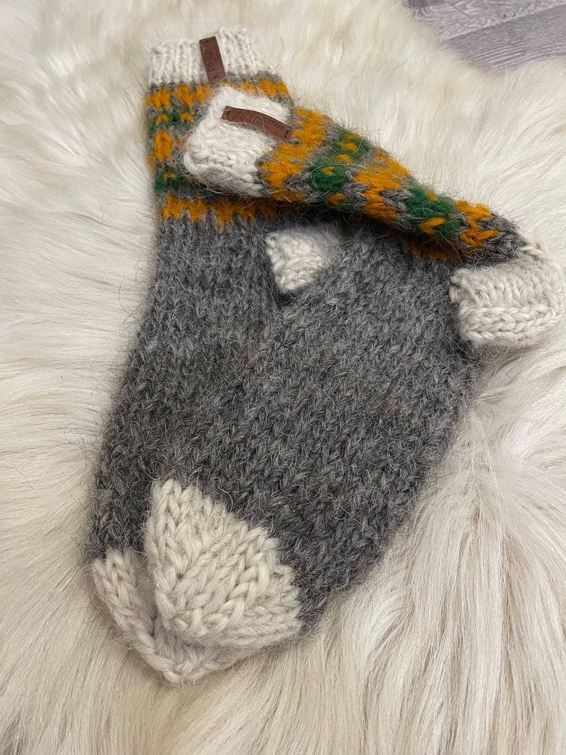 May include: A pair of grey, white and yellow knitted socks with a brown leather tag. The socks are made from a soft, fuzzy yarn.