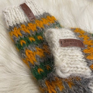 May include: A pair of knitted fingerless gloves with a white, grey, green, and yellow striped pattern. The gloves have a brown leather tag with the text "SOUVENIR" on them.