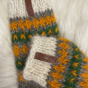 May include: A pair of knitted wool socks with a colourful geometric pattern in shades of white, grey, green, and orange. The socks have leather tags that say "Souvenir" and "Canada".