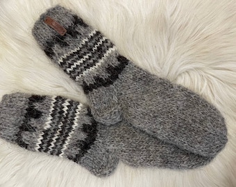 Puede incluir: Un par de guantes de lana grises con un patrón geométrico blanco y negro. Los guantes tienen una etiqueta de cuero marrón con la palabra "SUOMIKKA" en ella.