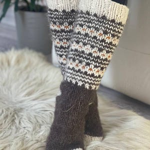 Puede incluir: Calentadores y calcetines de punto hechos a mano. Los calentadores tienen una parte superior e inferior de color crema con un patr&oacute;n geom&eacute;trico en marr&oacute;n y blanco. Los calcetines son de color marr&oacute;n liso con una puntera color crema. Los calentadores miden unos 30 cm de largo.