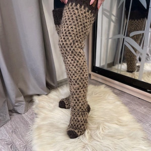 Peut inclure: Jambières hautes au genou avec un motif pied-de-poule marron et beige. Le haut et le pied sont marron foncé uni. Les jambières sont faites d'un matériau tricoté épais et texturé.