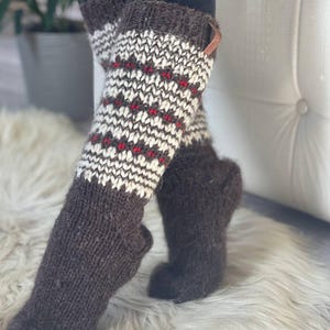 May include: Knee-high knit socks in brown, white, and red. The socks feature a patterned design on the upper portion and a solid brown color on the foot. A small leather tag is attached to the top of one sock.