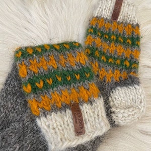 May include: A pair of grey, green and orange striped wool knit fingerless gloves with a white cuff. The gloves have a brown leather tag that says "Souvenir" on it.