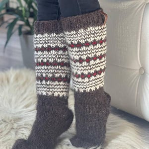 May include: Knee-high knit socks in brown, white, and red. The socks feature a patterned design with a brown cuff and foot. The socks are made of a thick, warm material.