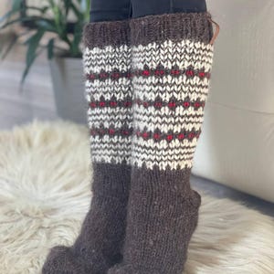 May include: Knee-high wool socks in brown, white, and red. The socks have a patterned design on the upper portion and a solid brown foot. The socks are thick and appear warm, suitable for cold weather.
