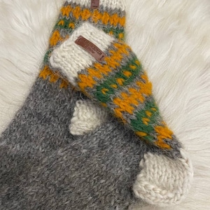 May include: A pair of grey, green and orange knitted wool socks with a white cuff. The socks have a brown leather tag with the text "Alpaca" on them.