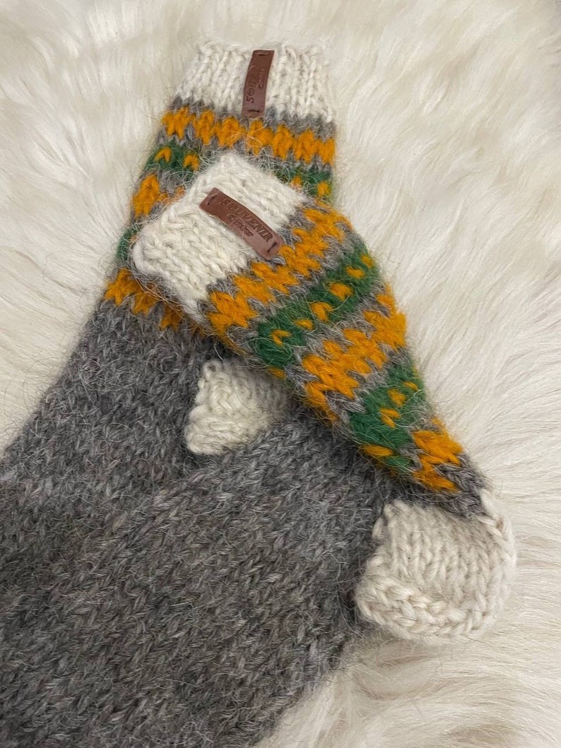 May include: A pair of grey, green and orange knitted wool socks with a white cuff. The socks have a brown leather tag with the text "Alpaca" on them.