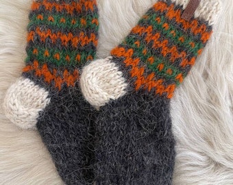 May include: A pair of hand-knitted wool socks. The socks have a grey foot and a cream-coloured cuff and toe. The upper portion of the socks has a pattern of orange and green zigzags. A small brown leather tag is attached to the cuff.