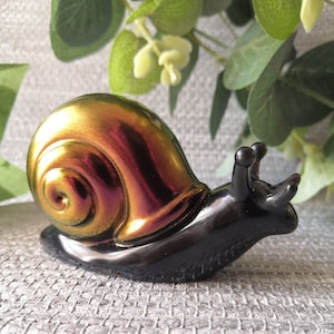 May include: A black and iridescent snail figurine with a gold and purple shell. The snail is made of glass and has a smooth, glossy finish.