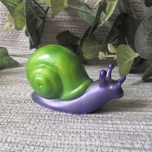 May include: A green and purple snail figurine with a shiny finish. The snail's shell is green and the body is purple.