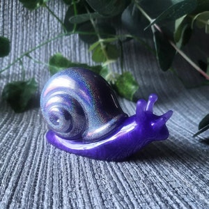 May include: A purple and iridescent snail figurine with a glittery shell. The snail is made of resin and has a glossy finish.