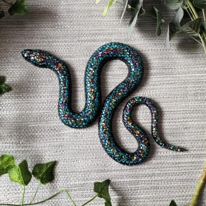 May include: A turquoise and black iridescent snake figurine with a glittery finish.