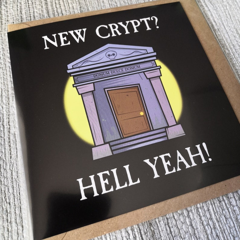 Pu&ograve; includere: Un biglietto di auguri in bianco e nero con un'illustrazione a fumetti di una cripta con il testo "NEW CRYPT? HELL YEAH!" e la frase latina "DOMUM DULCE DOMUM" sopra la porta.