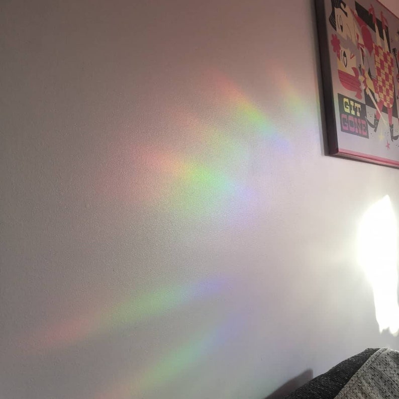 May include: A white wall with a rainbow prism light reflection. The light is coming from a window and creating a rainbow effect on the wall. There is a framed picture on the wall with the text "Get Gone" on it.