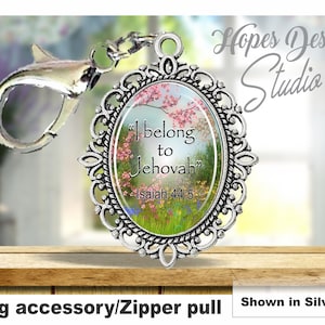 以下が含まれることがあります： 花柄のデザインと「私はエホバに属している」というテキスト（イザヤ 44:5）が刻まれたシルバーチャーム。バッグアクセサリーやジッパーの引き手として使用できます。