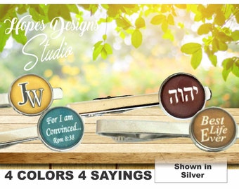 May include: Four tie clips with different designs. The first tie clip has a yellow background with the initials "JW" in white. The second tie clip has a teal background with the text "For I am Convinced... Rom 8:38". The third tie clip has a brown background with the Hebrew word "יהוה" in white. The fourth tie clip has a tan background with the text "Best Life Ever". All tie clips are shown in silver.