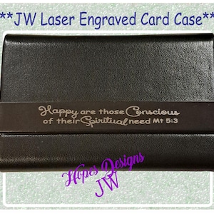 Könnte beinhalten: Schwarzes Kartenetui mit strukturierter Oberfläche. Ein dunkelbraunes Band umschließt die Mitte, graviert mit dem Text "Happy are those Conscious of their Spiritual need Mt 5:3". Der Text "JW Laser Engraved Card Case" steht oben.