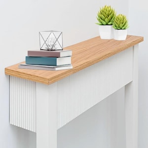 May include: A contemporary console table in white and wood, featuring a slatted front. It's adorned with books, a geometric glass terrarium, and two small potted succulents. The table's dimensions are not visible.