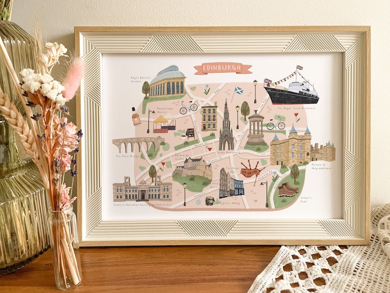 May include: A colorful illustrated map of Edinburgh, Scotland, with landmarks like Edinburgh Castle, the Royal Yacht Britannia, and the Sheep Held Inn. The map is framed in a light wood frame.