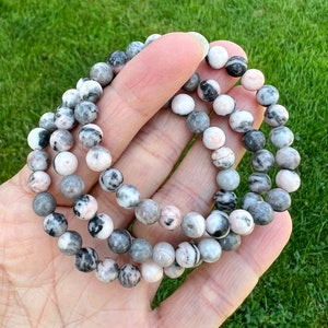 May include: A bracelet made of pink and grey gemstone beads. The beads are round and have a marbled pattern.