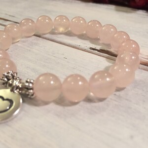May include: A pink rose quartz beaded bracelet with a silver heart charm. The bracelet is made with 8mm beads and is approximately 7 inches in length.