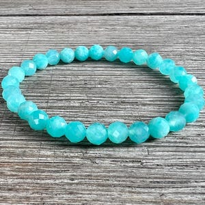 May include: A turquoise blue gemstone bracelet made of faceted beads. The bracelet is made of natural stones and is strung on elastic.