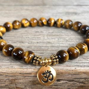 Op de afbeelding: Een bruin en gouden tijgeroog kralen armband met een gouden Om bedel.