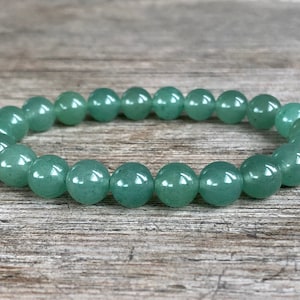 May include: A green gemstone bracelet made of round beads. The bracelet is on a wooden surface.