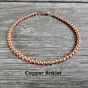 May include: A copper anklet made of small, round beads. The anklet has a lobster clasp closure.