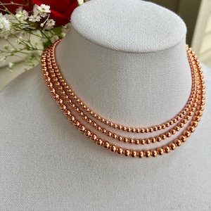 May include: A layered necklace made of three strands of copper beads. The beads are round and have a shiny, metallic finish.
