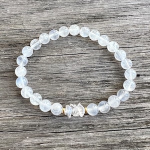 Peut inclure: Un bracelet en perles de cristal blanc avec un fermoir doré et un charme en cristal de quartz transparent.