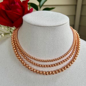 May include: A layered necklace made of three strands of copper beads. The beads are round and have a shiny, metallic finish.