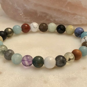 May include: A bracelet made of various colored beads, including white, black, brown, green, blue, and purple. The beads are strung on a clear elastic cord.