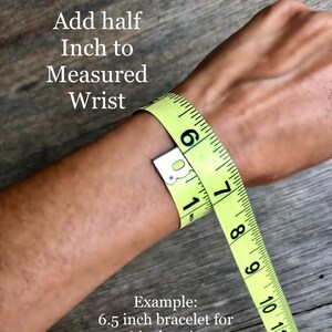 May include: A yellow measuring tape wrapped around a wrist to demonstrate how to determine bracelet size. The text reads "To Determine Bracelet Size", "Add half Inch to Measured Wrist", and "Example: 6.5 inch bracelet for 6 inch wrist".