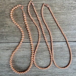 May include: Three copper beaded necklaces of varying lengths. The necklaces are made of small, round beads and have a simple, elegant design.