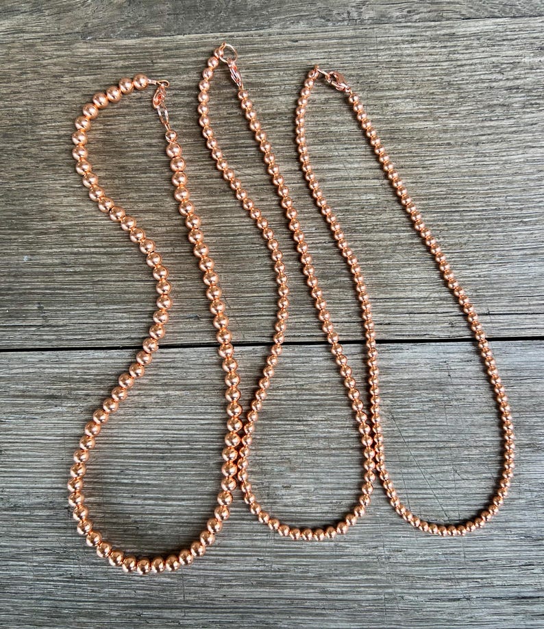 May include: Three copper beaded necklaces of varying lengths. The necklaces are made of small, round beads and have a simple, elegant design.