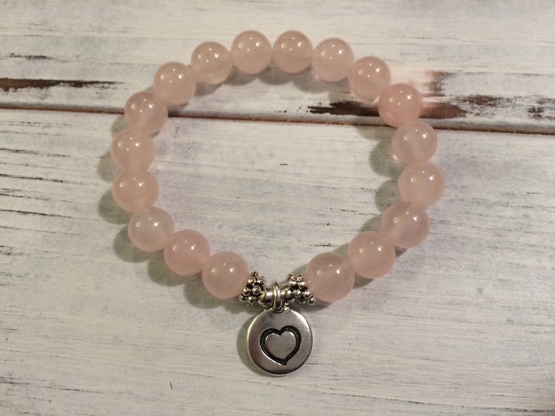 May include: A pink rose quartz bracelet with a silver heart charm. The bracelet is made of round beads and is strung on elastic.