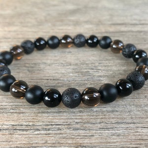 May include: A black beaded bracelet with brown and black beads. The bracelet is made of agate, lava rock, and smoky quartz.