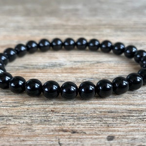 May include: A black beaded bracelet made of round, polished stones. The bracelet is on a wooden surface.