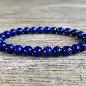 Op de afbeelding: Een blauwe armband van ronde stenen kralen. De armband ligt op een houten oppervlak.