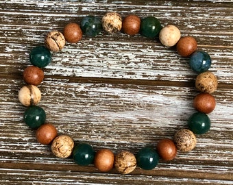 May include: A bracelet made of brown wood, green, and white agate beads. The bracelet is on a wooden surface.