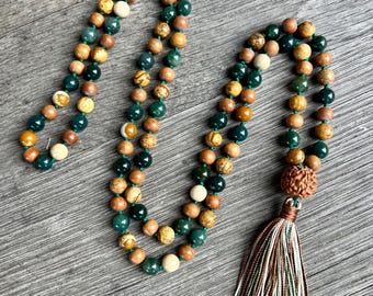 May include: A green, brown, and white beaded mala necklace with a tassel. The mala is made of natural stones and has a wooden bead at the end.