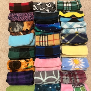 May include: A selection of fleece pouches in diverse patterns and colours, such as plaid, floral, and starry designs. The rectangular pouches have a folded flap closure, ideal for small items.
