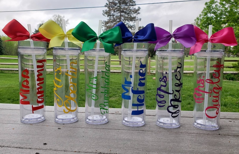 May include: Six clear plastic tumblers with straws and colorful bows. Each tumbler is personalized with a teacher's name, including "Miss Tammy", "Mrs. Oberlin", "Mrs. Burchholder", "Mr. Hefner", "Mrs. Meurer", and "Mrs. Quigley".