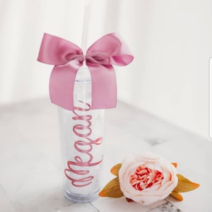 May include: A clear plastic tumbler with a pink ribbon bow and a straw. The tumbler has the name "Megan" written on it in pink lettering.