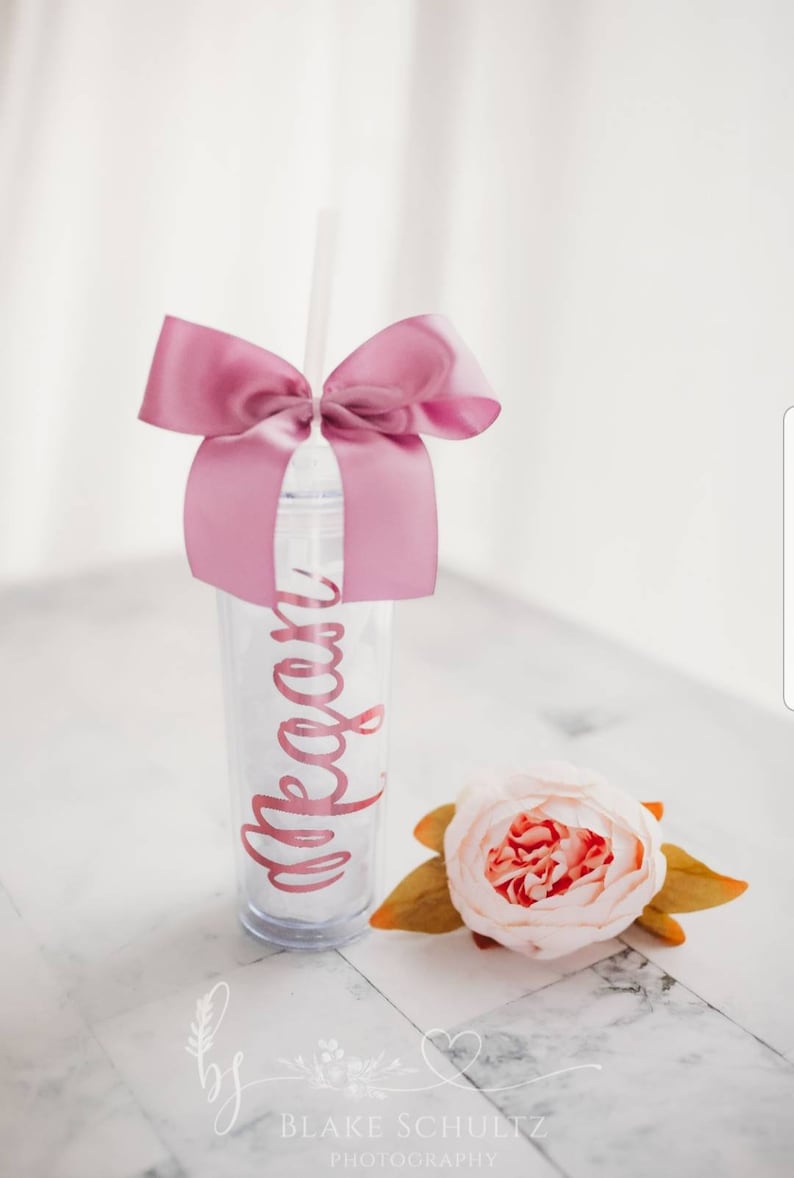 May include: A clear plastic tumbler with a pink ribbon bow and a straw. The tumbler has the name "Megan" written on it in pink lettering.
